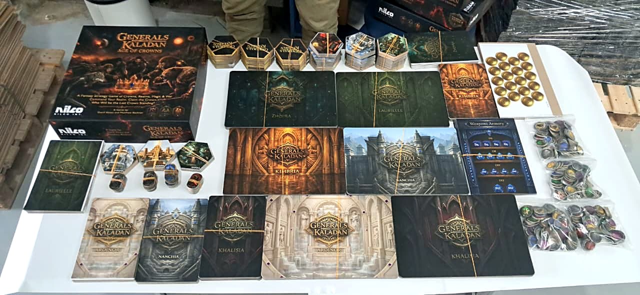 The box, realm boards, hex tiles, coins and army tokens laid out on a table at the factory